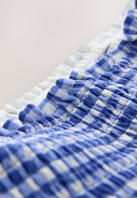 Primo piano di tessuto a quadri blu e bianco con elastico arricciato e bordo bianco arricciato su uno sfondo chiaro.