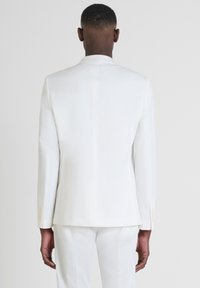Giacca bianca su misura, con una vestibilità slim, texture liscia, spacco singolo sul retro e bottoni chiari sulle maniche.