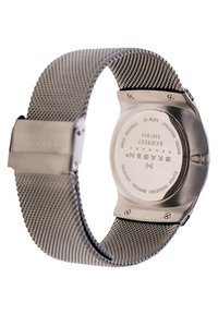 Zegarek na stalowej siatce z okrągłą kopertą. Tył zdobią grawerowane detale, wskaźnik wodoszczelności oraz szkiełko mineralne.