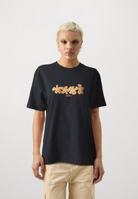 Black cotton t-shirt with a relaxed fit, featuring orange floral designs across the chest and a small logo beneath the flowers.