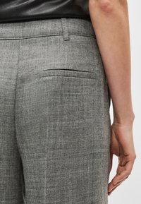 Calças cinzentas feitas à medida em tecido texturizado, com um bolso traseiro e um cós liso, detalhes de costura visíveis.