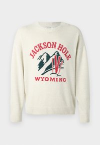 Jasna kremowa sweter z grubym splotem. Posiada graficzny wzór z napisem "JACKSON HOLE" i "WYOMING" w kolorach czerwonym i zielonym. Okrągły dekolt.