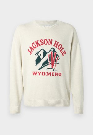 Light cream sweater with a chunky knit texture. Features a graphic design with "JACKSON HOLE" and "WYOMING" in red and green. Round neckline.