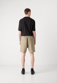 Black short-sleeve shirt with a relaxed fit, paired with beige, knee-length shorts featuring an elastic waistband and two back pockets.