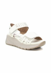 Sandalias de cuña sintéticas blancas con tiras perforadas y cierres de Velcro, que cuentan con un suave forro interior y una suela en un tono beige claro.