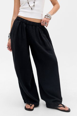Personne portant un pantalon noir ample, un débardeur blanc court, des tongs, ainsi que plusieurs bagues, bracelets et colliers, avec des tatouages sur les bras.
