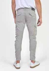 Lichtgrijze cargo broek met slim fit, met twee zijzakken en twee achterzakken. Gediend met witte sneakers op een effen achtergrond.
