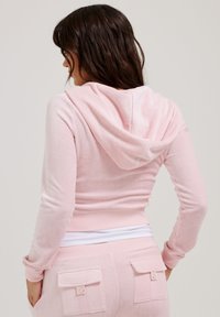 Rožinė džemperio su gobtuvu ilgomis rankovėmis ir figūrą glotninančiu dizainu. Minkšta tekstūra, juostuota apačia ir išryškintos kišenės ant atitinkančių kelnių.