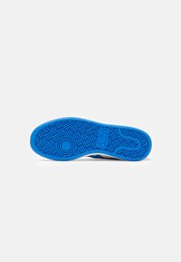 Suola di sneaker in gomma blu con un motivo di presa testurizzato e accenti circolari. Bordi lisci, con una parte superiore bianca.