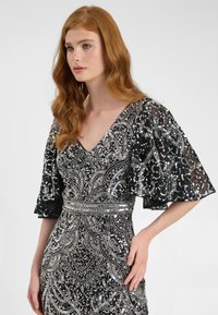 Abito nero con decorazioni argento, scollatura a V e maniche corte a campana. Dettagliato con motivi intricati e vita strutturata.