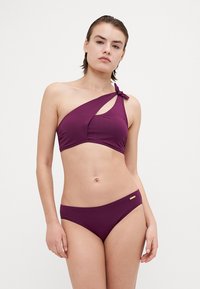 Set bikini in un profondo viola, con un top a spalla unica con dettaglio annodato e slip a taglio classico. Tessuto morbido e elasticizzato. Accento dorato sui slip.
