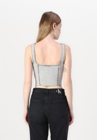 Top in denim accorciato di colore azzurro chiaro con spalline spesse e schiena quadrata; abbinato a jeans neri con una patch del logo e tasche cucite.