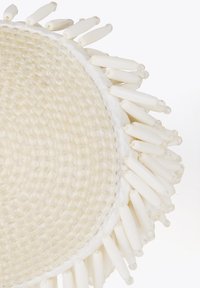 Okrągły biały pleciony podkładka z błyszczącymi akcentami, z koralikowym brzegiem i cylindrycznymi białymi detalami, tworzącymi teksturowaną powierzchnię.