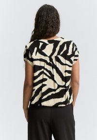 Blouse rayée noir et crème avec des manches courtes, un décolleté arrondi et un détail froncé à l'arrière. Texture de tissu lisse.