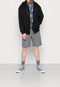 Black zip-up hoodie, blue patterned t-shirt, gray shorts, blue high-top sneakers, gray socks. Casual outdoor outfit with layered textures.