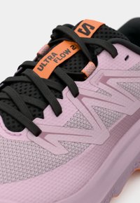 Ανοιχτό μωβ παπούτσι για τρέξιμο με πλέγμα στην επάνω επιφάνεια, μαύρες λεπτομέρειες και πορτοκαλί ετικέτα. Διαθέτει υλικά με υφή και ξεχωριστό λογότυπο στο πλάι.