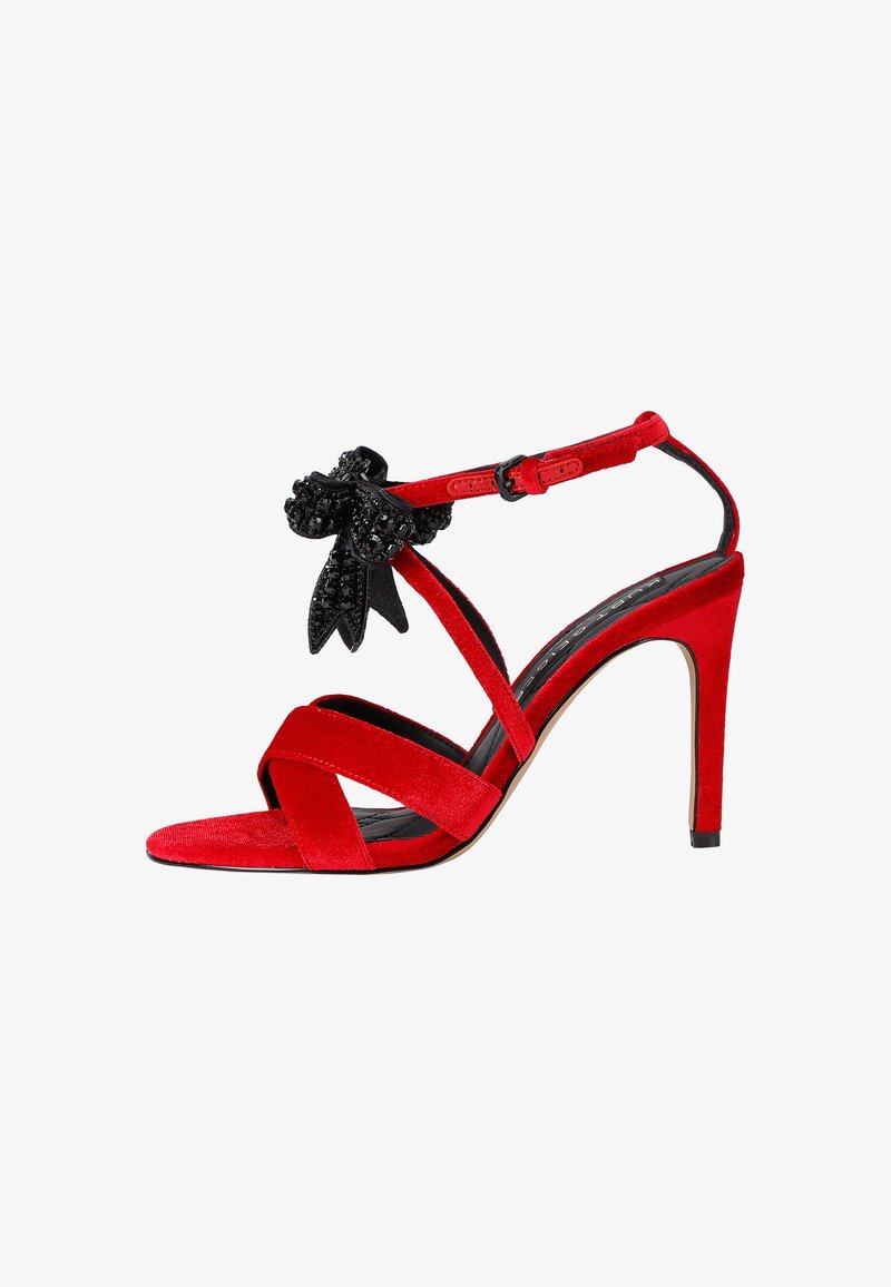 Czerwone zamszowe sandały na wysokim obcasie z wieloma krzyżującymi się paskami, zdobione czarnym akcentem w postaci kwiatu, z zapięciem w kostce.