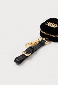 Bolsa redonda de chave em veludo preto com fecho dourado. Apresenta uma alça em couro preto e acessórios dourados. Detalhe de monograma na parte superior.