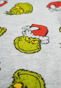 Il tessuto grigio presenta una stampa ripetitiva del personaggio del Grinch che indossa un cappello da Babbo Natale rosso, con occhi gialli e pelliccia verde.