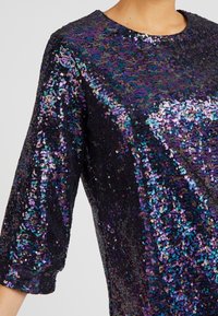 Black, sequin-covered top featuring a round neckline and three-quarter length sleeves, reflecting purple and blue hues.