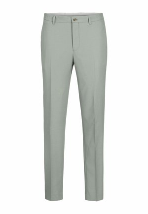 Osoba ubrana w jasnoszary garnitur, białą koszulkę i białe trampki z czarnymi akcentami, stojąca na jednolitym tle.