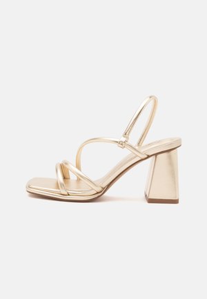 Kuldne rihmik sandaal ruudukujulise lahtise ninaga, slingback-rihmaga ja robustse plokkkontsa, näidatud heledal ühtlasel taustal.