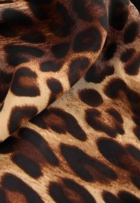Leopardimustriga kangas, millel on sile tekstuur, pruunid ja mustad laigud korallika taustal, esindades julgeid mustreid ja voolavat langust.