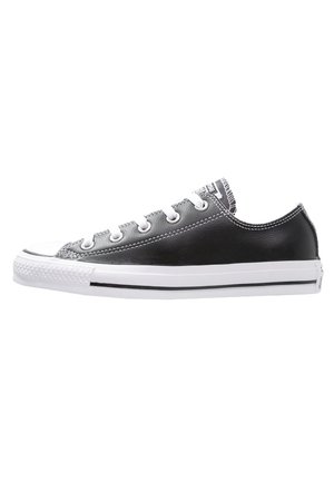 Baskets basses en cuir noir avec semelle en caoutchouc blanche, lacets blancs et couture contrastée. Bout rond classique et logo sur la languette.