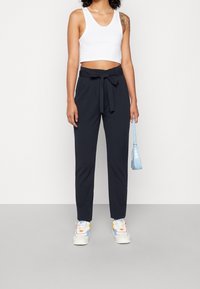 Pantalons navy à taille haute avec ceinture à nouer, associés à un crop top blanc. La tenue est complétée par des baskets blanches et un sac à main bleu clair.