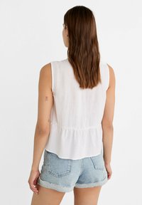 Biała, bezrękawnikowa bluzka z marszczonym stanikiem, wykonana z lekkiego materiału. Połączona z krótkimi niebieskimi szortami dżinsowymi z podwiniętymi końcami.