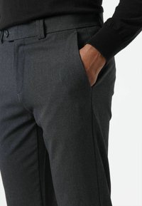 Dunkelgraue, maßgeschneiderte Hose mit glatter Textur, ausgestattet mit Seitentaschen und schlankem Schnitt. Sichtbare Steppnähte entlang der Nähte.