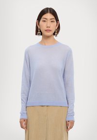 Pull en tricot bleu clair avec des manches longues, col et ourlet côtelés. Texture douce, associé à une jupe en velours côtelé beige pour le contraste.