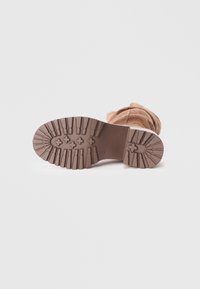 Botine din suede, cu vârful rotund, de culoare brown, cu talpă din cauciuc flexibilă, având un profil adânc pentru aderență și un superior din material textil cu detaliu pliat.