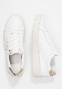 Vita lädersneakers med texturerade sulor, platta snören, stjärnformade utskärningar på ena sidan och gyllene accenter vid hälen. Rundad tådesign.