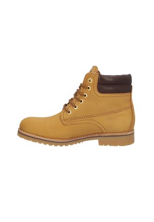 Bota de trabajo de cuero caqui con cuello acolchado oscuro, ojales de metal y suela gruesa de goma vista desde el lado interior sobre fondo blanco.