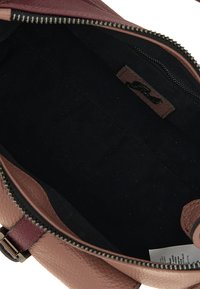 Interno della borsa in pelle, rivestimento in tessuto scuro, chiusura con zip, accenti bordeaux e una superficie esterna texture. Include etichetta del marchio sul lato.