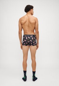 Schwarze Boxershorts mit einem Weihnachtsmann-Muster, elastischer Bund mit "JACK & JONES", getragen mit dunklen Socken mit einem grünen Blattdesign.