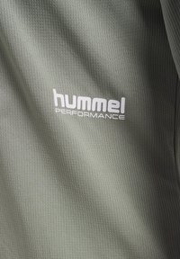 Grüner strukturierter Stoff mit einem gerippten Muster; verfügt über ein weißes "hummel PERFORMANCE"-Logo.