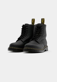 Zwarte leren veterschoenen met gele stiksels en zwarte zolen, voorzien van gele en zwarte merktabs aan de achterkant.