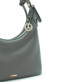 Sac hobo en cuir gris avec une finition texturée, de forme arrondie, accents en métal doré, et une étiquette de logo circulaire attachée à la sangle.