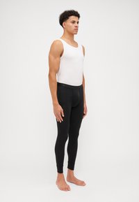 Black leggings with a fitted design, featuring a smooth texture and an elastic waistband, worn with a white tank top, on a barefoot model.