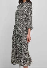 Middellange jurk met zwart-wit patroon, een kraag, driekwarts pofmouwen, een geplooide taille en een volant onderzoom.