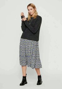 Dunkelgrauer gestrickter Pullover kombiniert mit einem fließenden Midirock im floralen Druck in Blau, Gelb und Weiß; schwarze Knöchelstiefel.