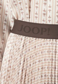 Tissu plissé avec un fond beige présentant un motif répétitif marron de éventails et de points. La ceinture est marron foncé avec "JOOP!" embossé.