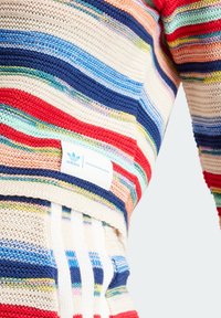 Suéter de punto de rayas multicolores que presenta tonos de azul, rojo, crema y verde. Incluye una etiqueta con logo y un diseño de tejido texturizado.