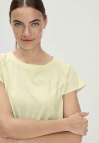 lichtgele katoenen T-shirt met korte mouwen, een brede ronde halslijn en een zachte textuur. Heeft een casual ontwerp met minimale details.