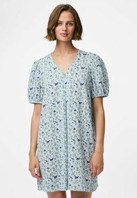 Vestido floral de color azul claro con mangas cortas abullonadas, escote en V y un ajuste relajado. Presenta pequeños patrones de flores verdes y moradas en todo el diseño.
