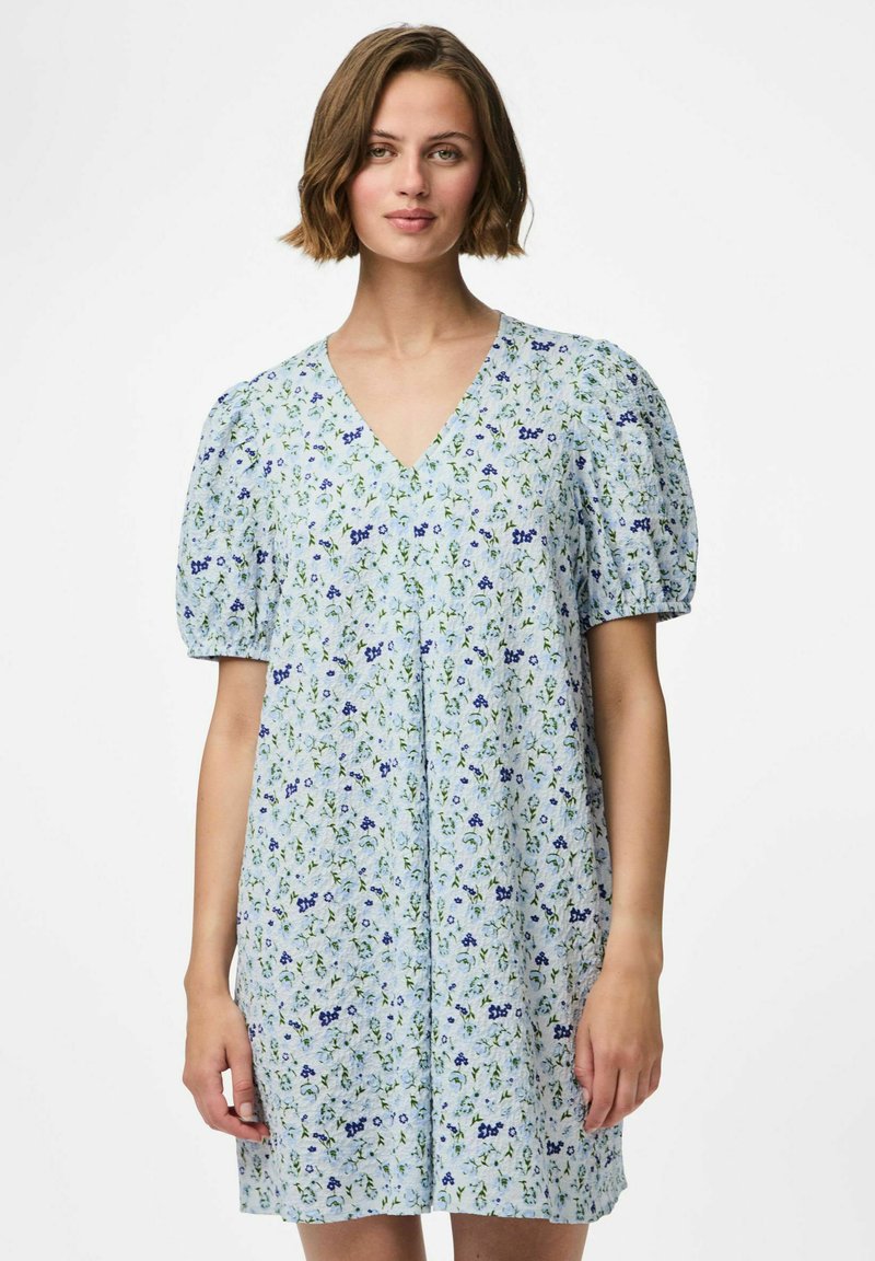 Vestido floral de color azul claro con mangas cortas abullonadas, escote en V y un ajuste relajado. Presenta pequeños patrones de flores verdes y moradas en todo el diseño.