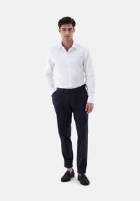 Weißes Button-Down-Hemd, marineblaue Anzughose, schlanke Passform, Baumwollstoff, glatte Textur, getragen mit lässigen schwarzen Schuhen.