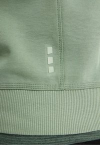 Primo piano di un tessuto a coste verde chiaro con una cucitura verticale e tre piccole toppe rettangolari riflettenti allineate verticalmente.